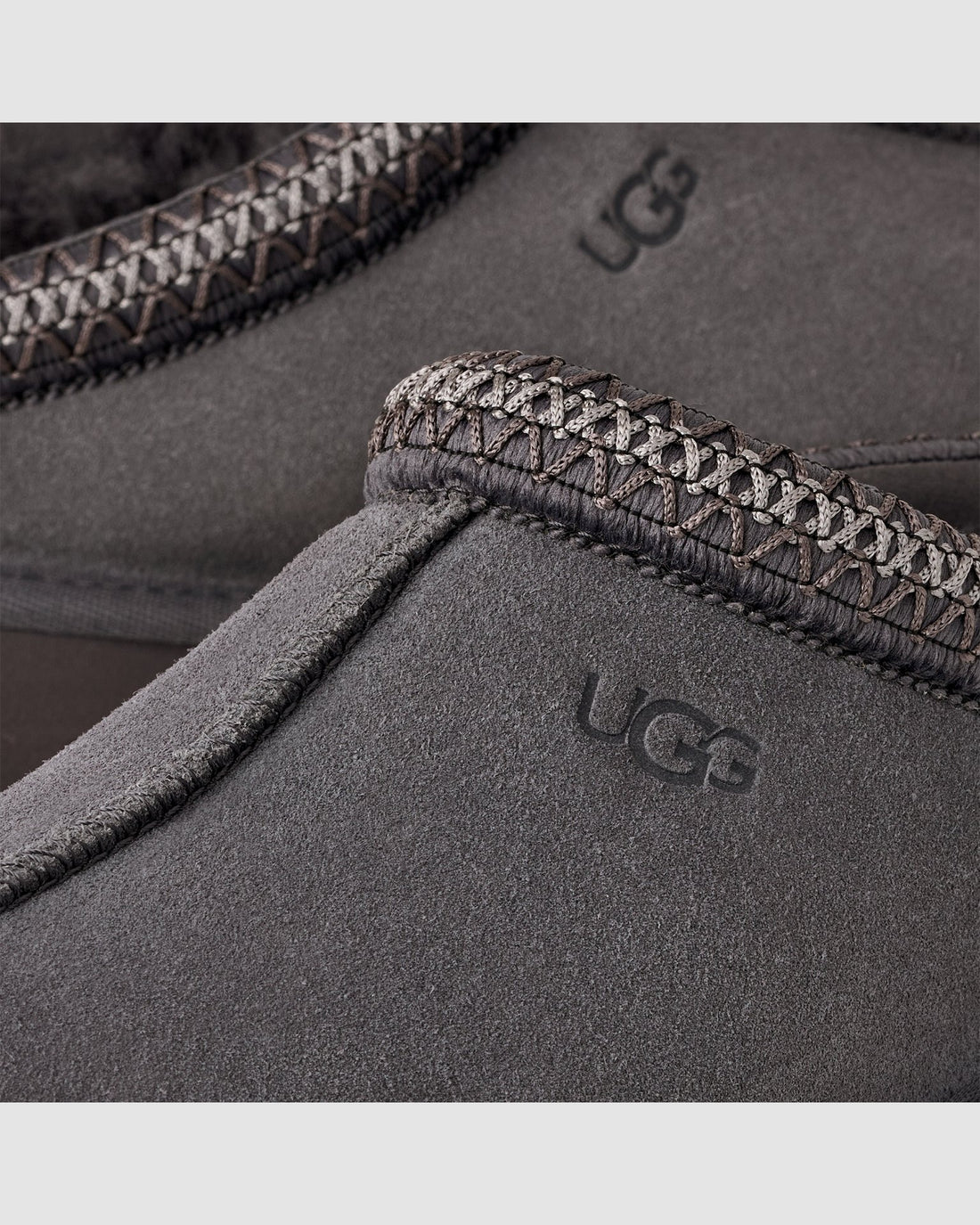 Close-up of UGG branded gray slippers with textured trim on a light gray background