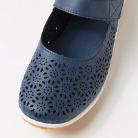 A close-up of a blue perforated Mary Jane shoe with a hook-and-loop strap, shown on a white background.