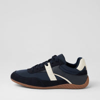 A low-top sneaker in navy blue suede and mesh with a contrasting off-white side stripe, navy heel tab, and a brown gum sole, shown from a side profile on a light gray background.