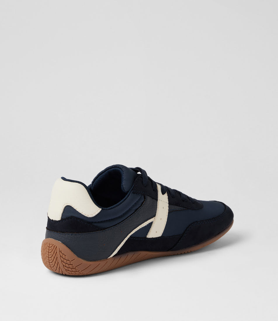 A low-top athletic sneaker shown from a rear three-quarter angle, featuring navy blue and off-white panels with a brown gum sole, set against a light gray studio background.