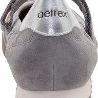 Close-up rear view of a gray suede shoe with a metallic silver heel tab, a dark strap, and the aetrex logo printed on the silver tab.